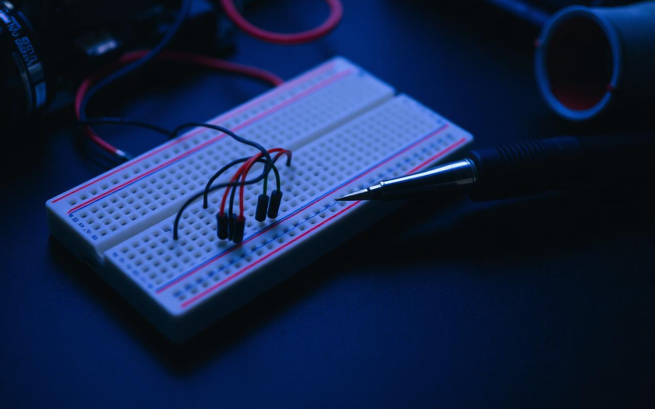 A breadboard with jumper wires beside a soldering iron on a dark workbench